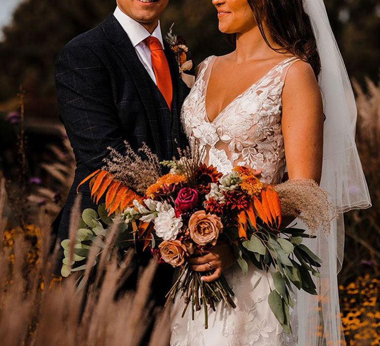 Oversized wedding bouquet with orange and red flowers with bride in lace wedding dress and floral hair accessories 