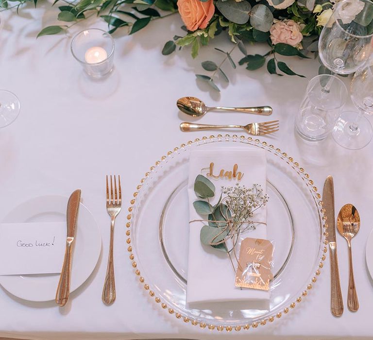 Gold, pink and green wedding place setting with personalised place name, foliage decoration and gold cutlery 