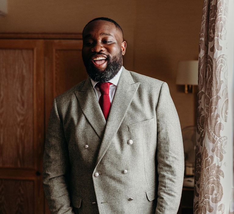 Groom wearing light grey double breasted suit jacket with bright red tie accessory 