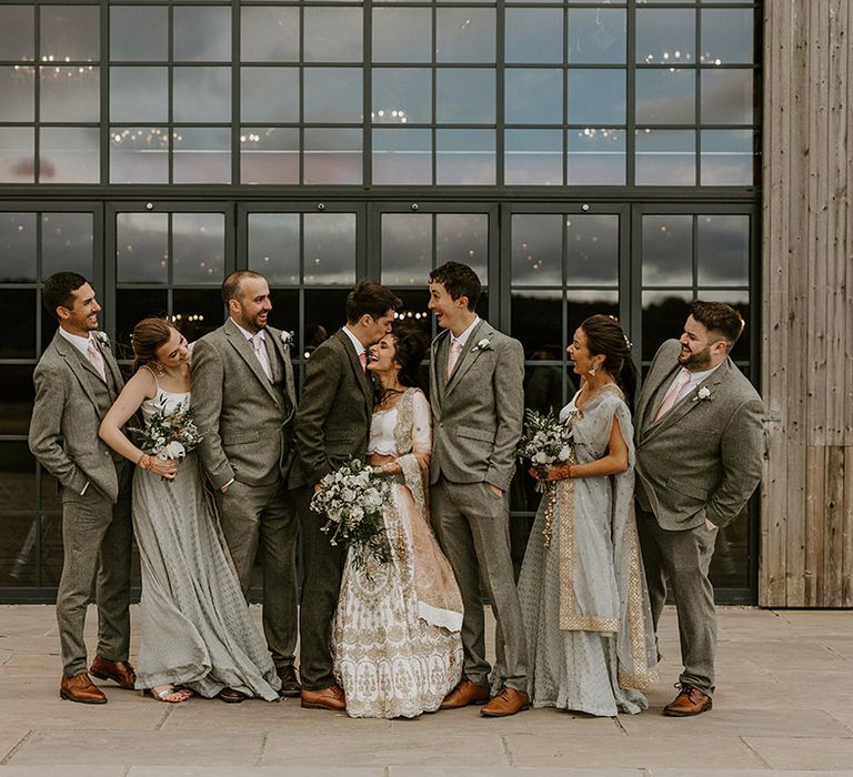 Group wedding photo of the whole wedding party with the bridesmaids and groomsmen in grey wedding outfits and bride and groom 