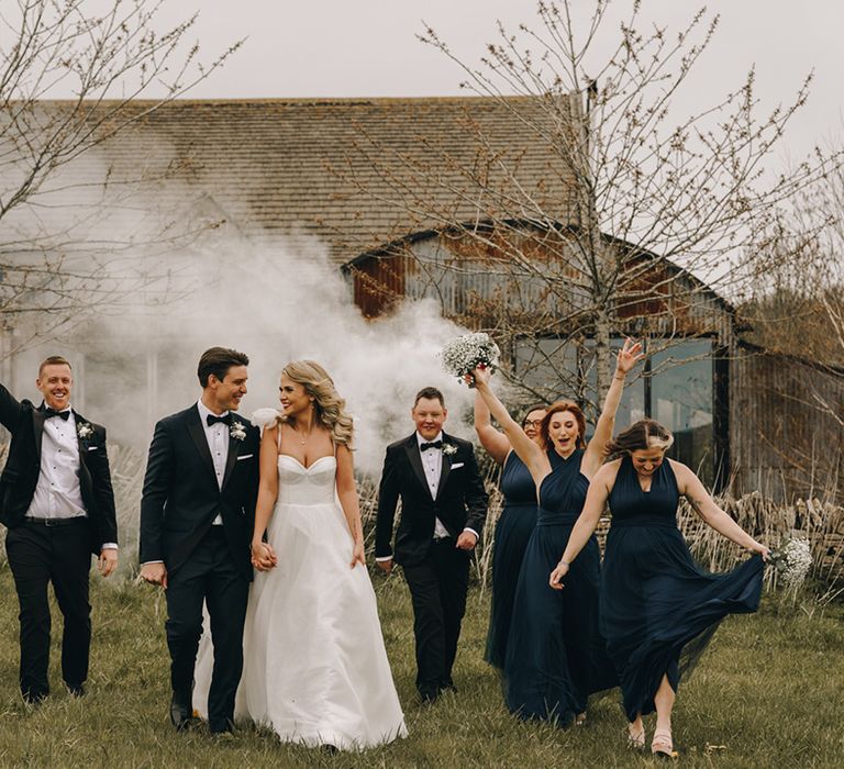 Wedding party wearing black tuxedos and nay bridesmaid dresses as they wave smoke bombs for Stone Barn country theme wedding