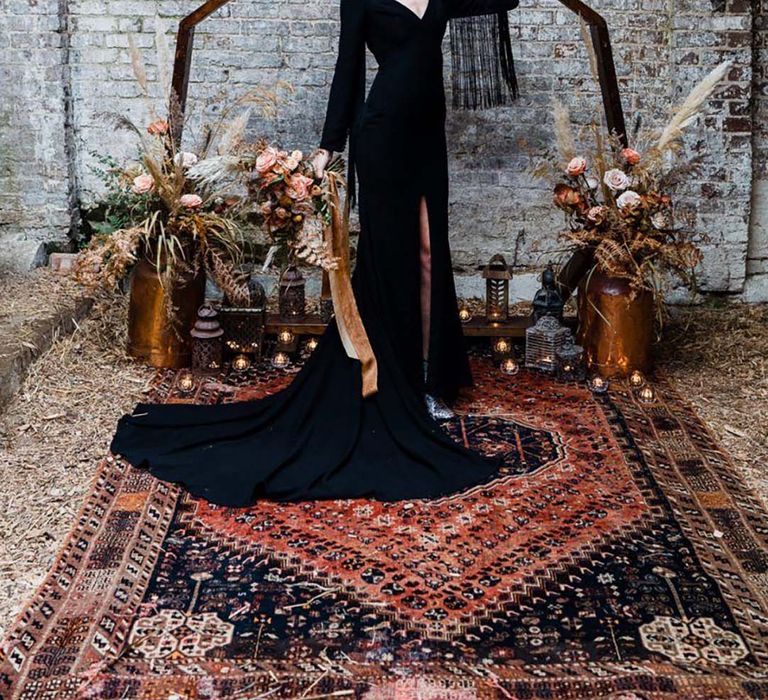 Bride in simple black wedding dress with black hat in front of moongate decoration for editorial shoot 