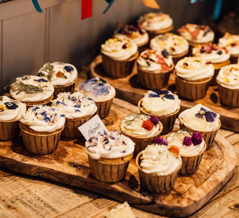 Wedding dessert table with cupcakes of different flavours decorated with edible flowers with rainbow wedding theme decorations and ribbons