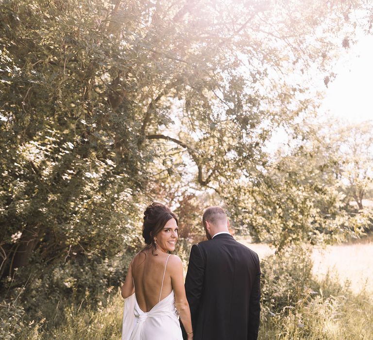 Bride in low back satin slip wedding dress walking with the groom during golden hour 