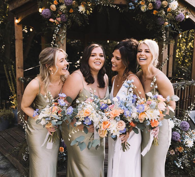 Pastel wedding theme for botanical wedding with the bridal party holding pastel wedding bouquets in sage green satin bridesmaid dresses 