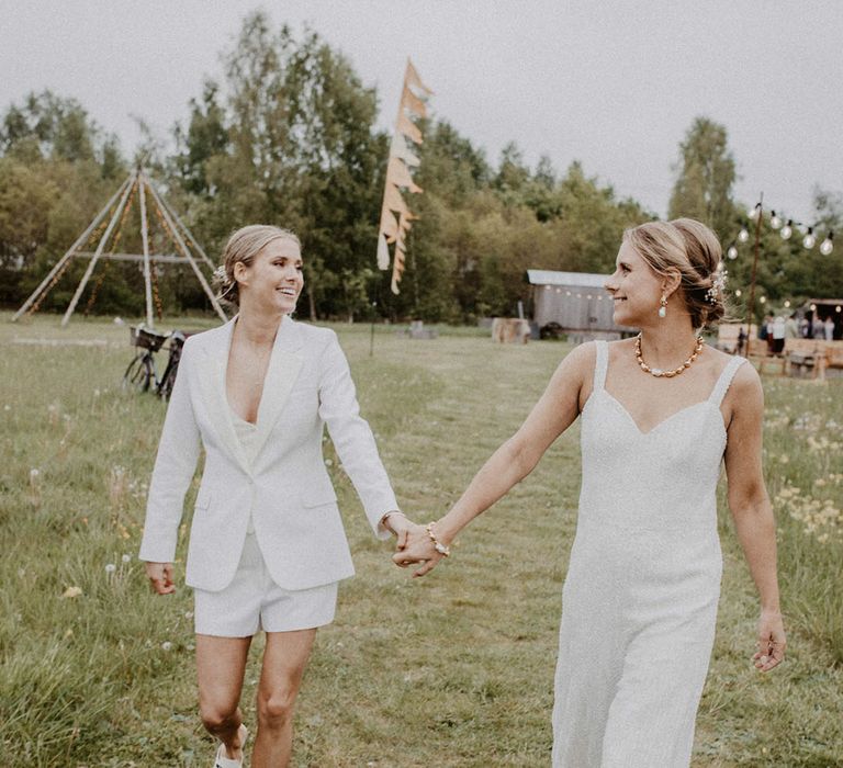 Bride in shorts, waistcoat and blazer with Gucci shoes walking with bride in sequin jumpsuit for the wedding reception 