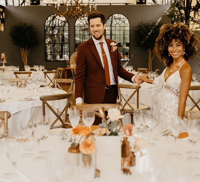 Bride in floral lace boho wedding dress with groom in red wedding suit walking around their Kent wedding venue 