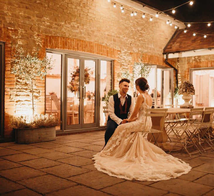 Bride and groom sitting outside Millbridge Court at evening reception with fairy lights 