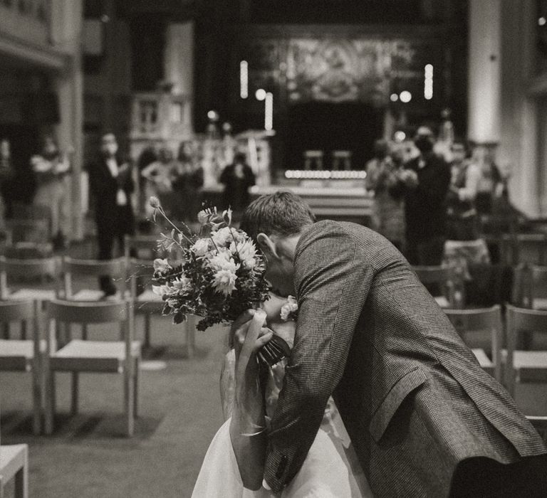 Groom in check blazer kissing his bride 