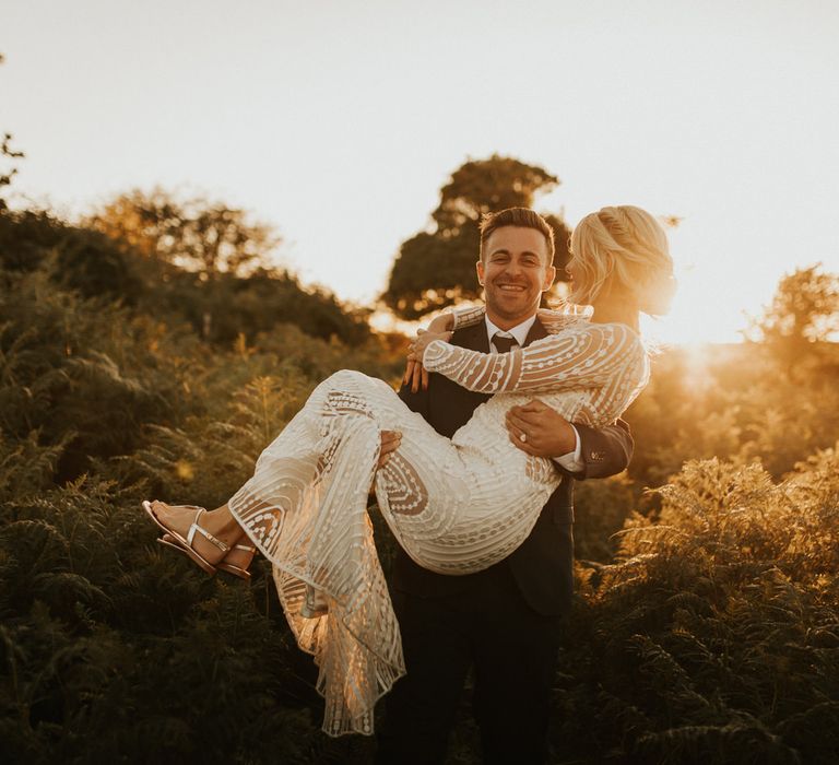 Golden hour portrait of the groom picking his bride up