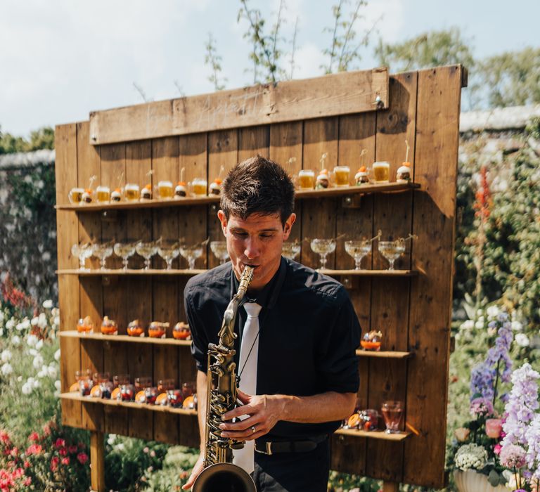 Saxophone player shares his music in front of rustic wooden bar and pastel flowers