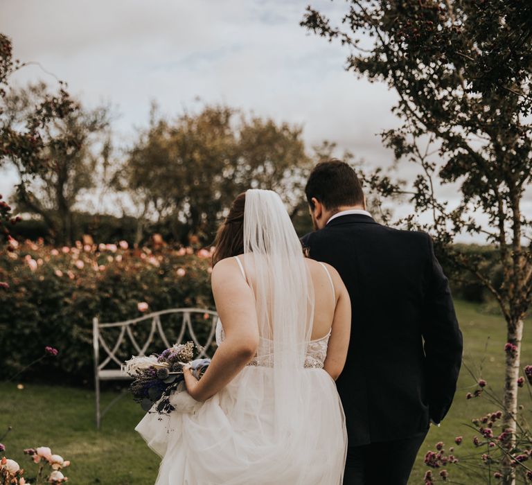 Bride with long veil walking in flower garden with groom