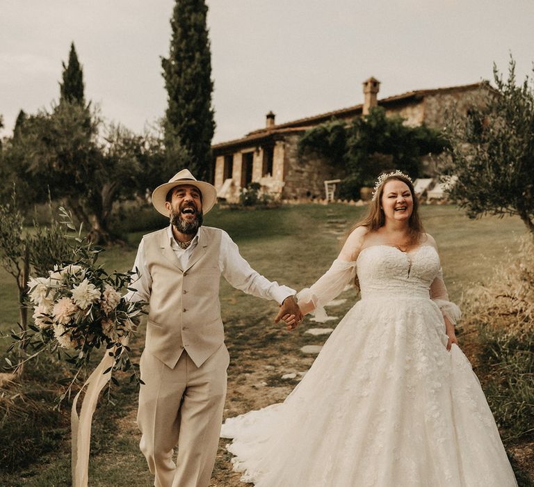 Bride and groom walking through Tuscany with olive bouquet