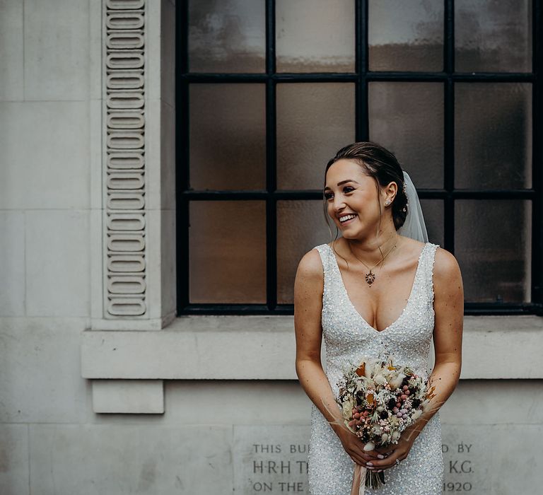 Pregnant bride in embellished wedding dress with dried flower bouquet 