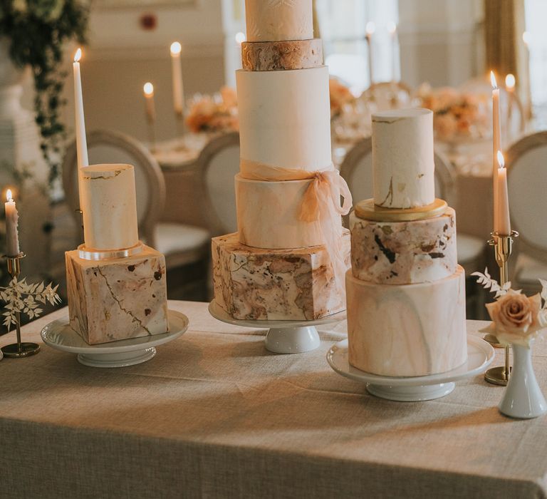 Three stylish wedding cakes with square and round layers in varying sizes and marble designs. 