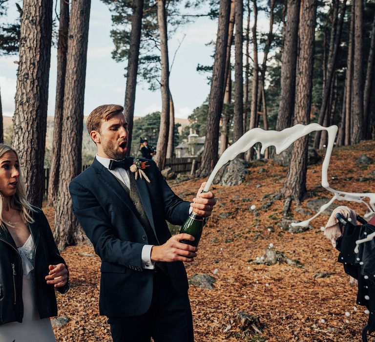 Groom pops champagne outdoors with bride on wedding day