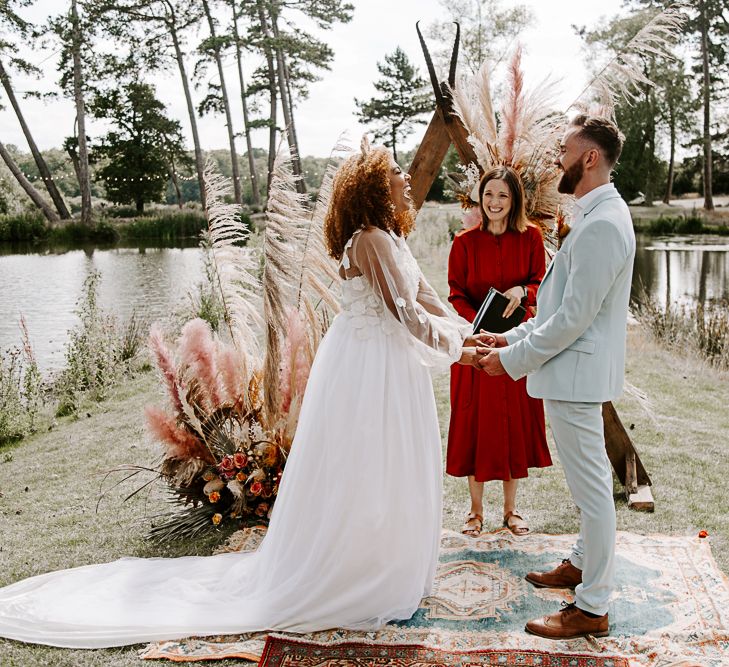 Bride & groom hold hands during wedding ceremony outdoors 