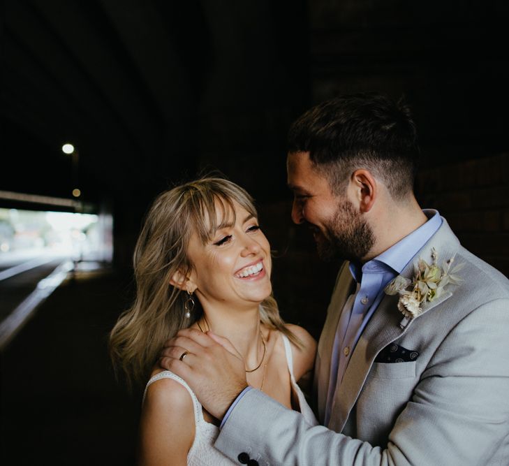 Couple portrait of white, blonde bride with fringe laughing and white groom with dark hair and grey suit