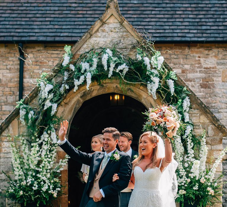 Newly wed couple at their church wedding in the countryside bride wears lace dress with peach wedding bouquet groom wears three-piece suit