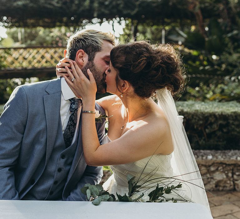 Bride with pinned up do kissing her groom in a blue wedding suit 