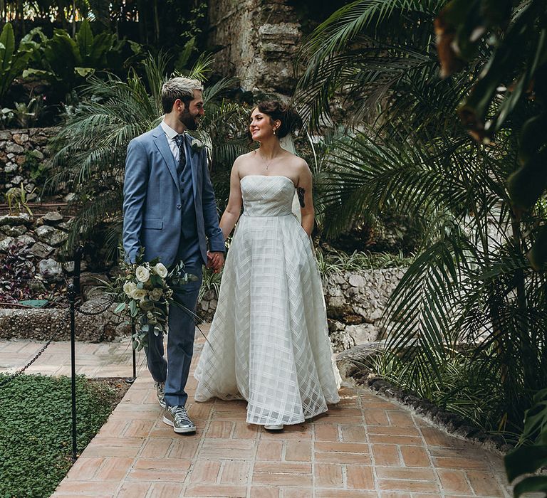 Bride in a strapless Wtoo wedding dress holding her grooms hand in a light blue suit at their Gibraltar Botanic Gardens elopement