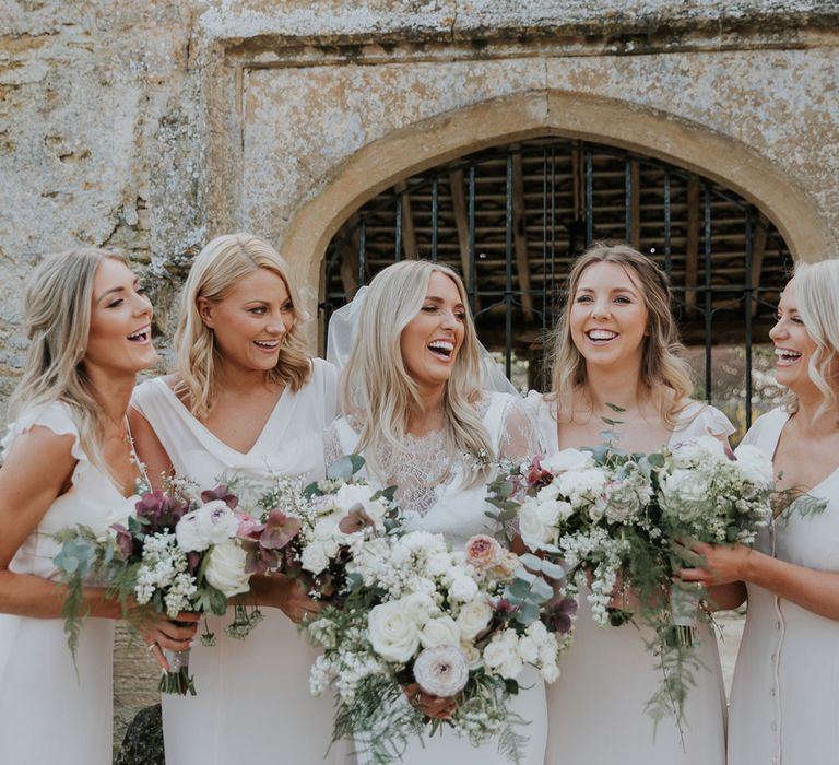 Laughing bride in white Charlie Brear dress and white lace Augusta Jones top standing with bridesmaids in silk ivory button dresses all holding white, pink and green wedding bouquets