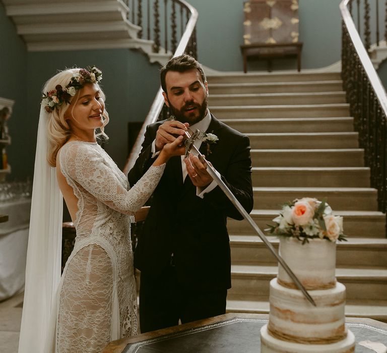 Bride in Grace Loves Lace wedding dress and single tier cathedral length veil and groom in black Hugo Boss suit cut rustic wedding cake with sword at Drenagh Estate Wedding