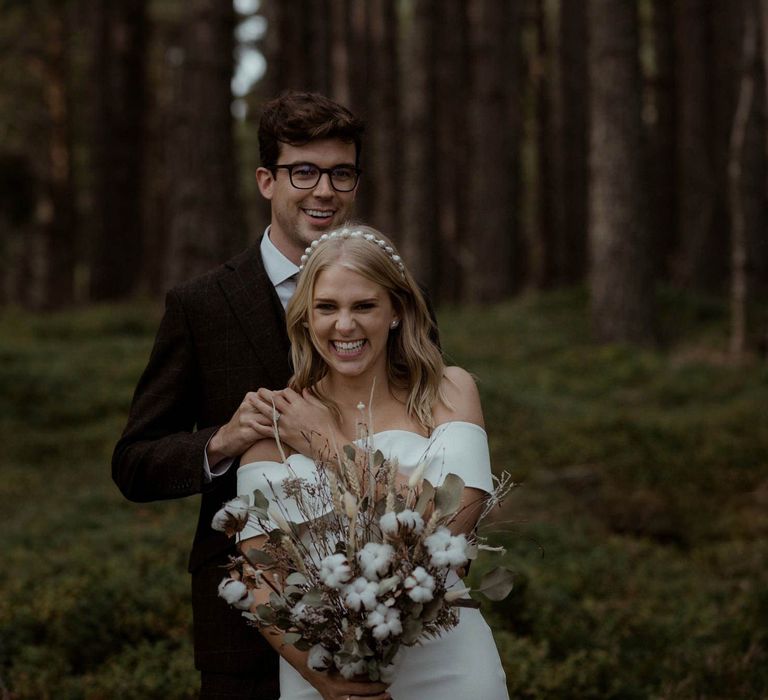 Bride & groom pose together whilst bride holds floral bouquet