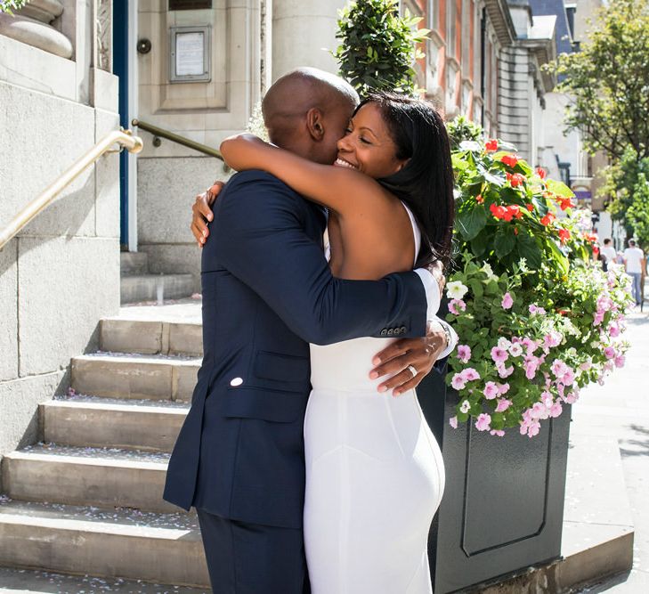 Bride in a fitted Roland Mouret dress embracing her new husband in a navy blue suit 