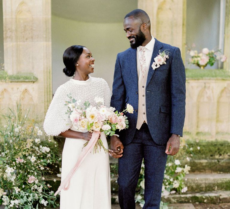 Bride and groom getting married at Barnsley House for romantic English garden party wedding, smiling and holding a white bouquet