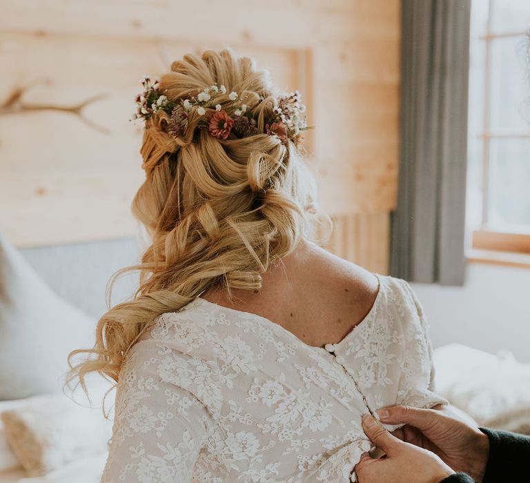 Bride with a half up half down wavy hairstyle decorated with fresh flowers having her wedding dress done up 