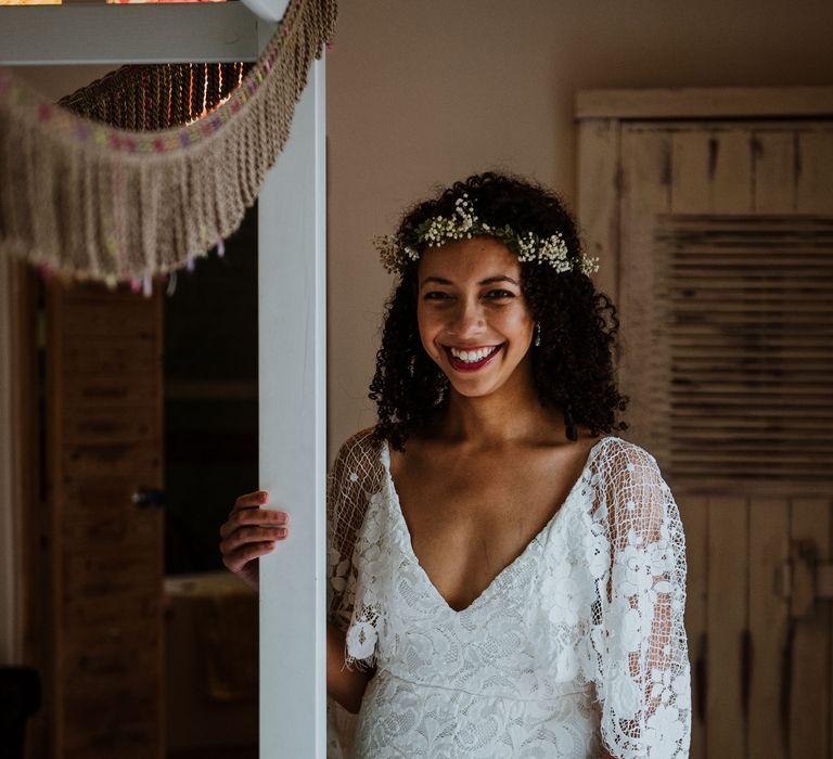 Bride stands and smiles at the camera whilst wearing red lipstick, simple floral crown, and Grace Loves Lace wedding gown