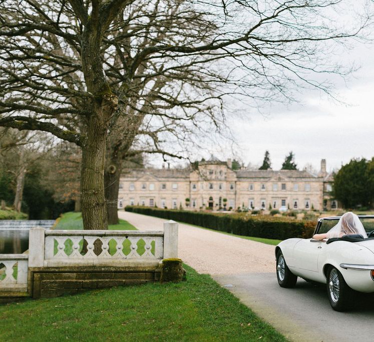 White convertible wedding car driving along Grantley Hall wedding venue's drive