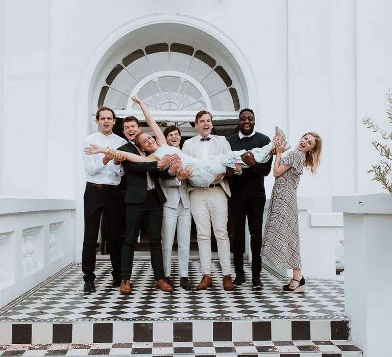 Wedding guests lift bride on the day of her wedding outside the Belair House