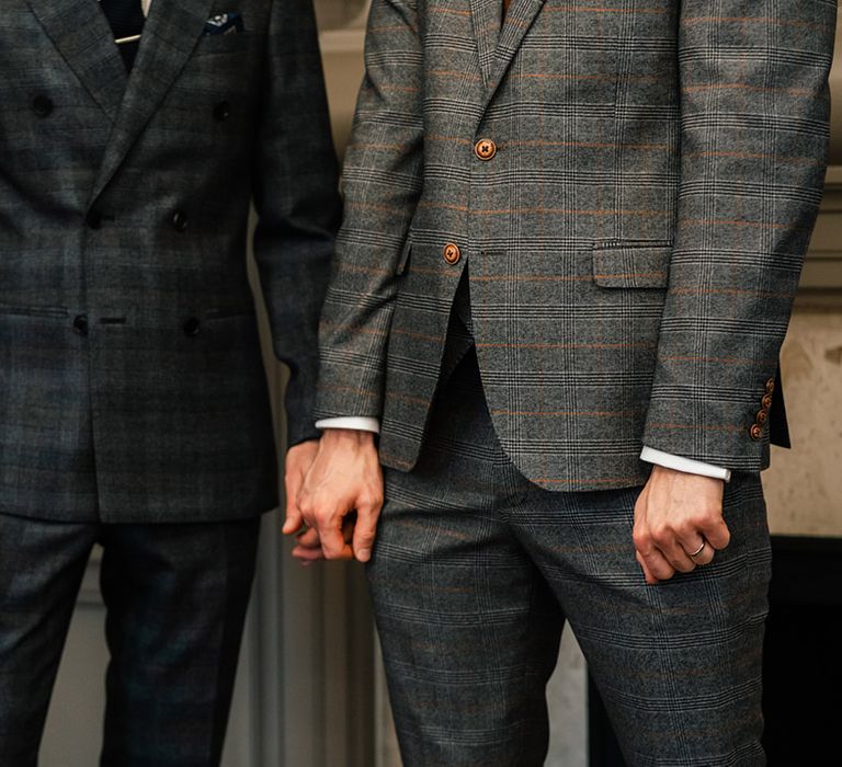 Grooms hold hands as they were stylish suits on their wedding day whilst stood outdoors after ceremony