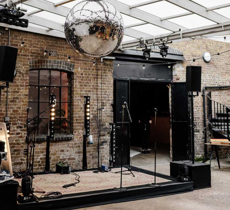 Stage in exposed brick courtyard with microphones, festoon lights and disco ball for wedding reception at Loft Studios London