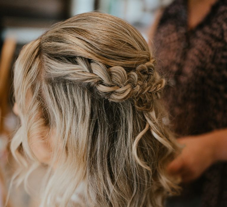 Bride with long blonde curled wedding hair and braids sits in chair before late summer wedding in Norfolk