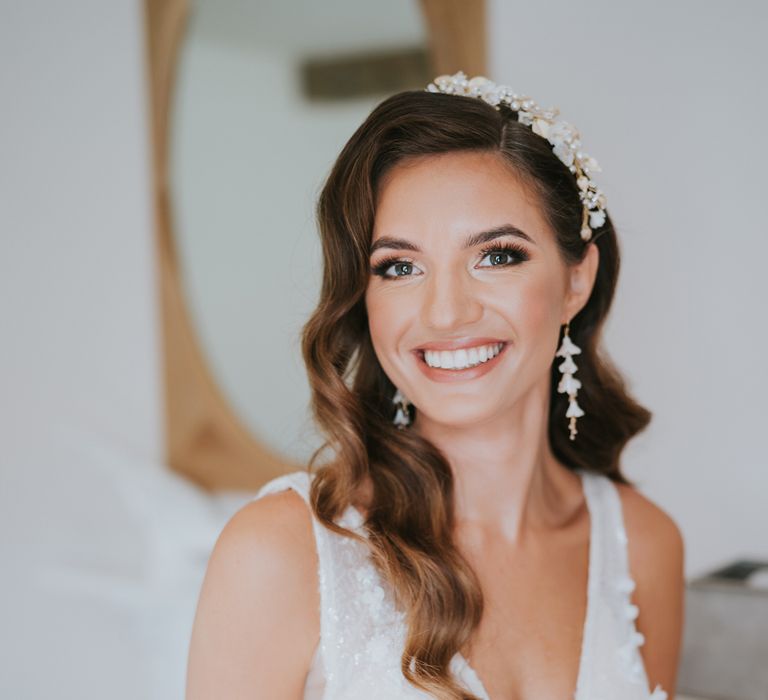 Smiling bride with curled hair and floral headband wearing Berta wedding dress with deep V neckline and applique flowers before summer wedding at Primrose Hill Farm