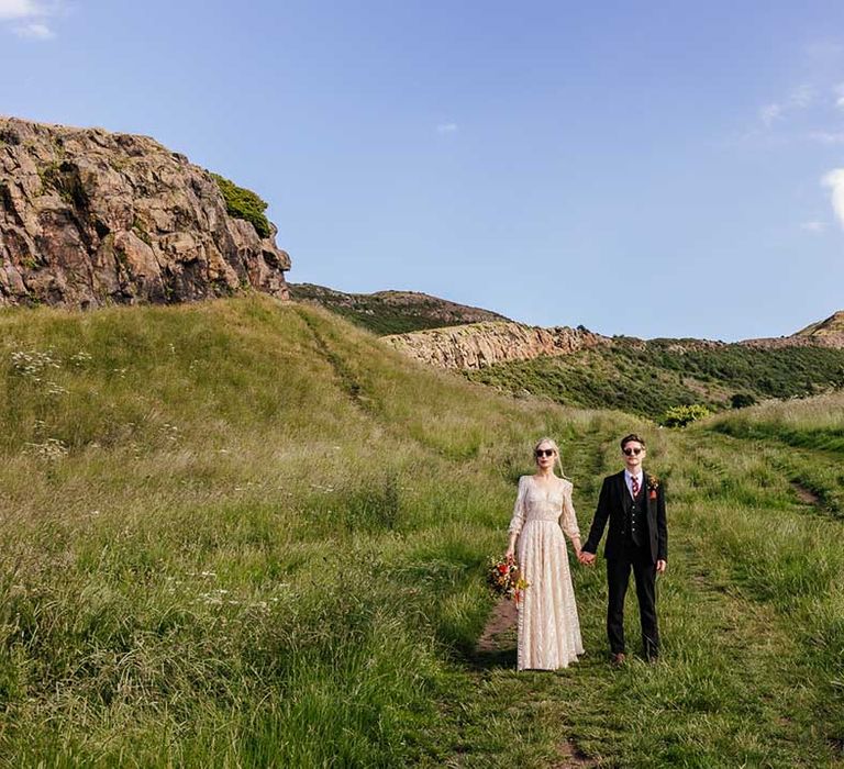 Bride & groom hold hands as they sun shines around them 