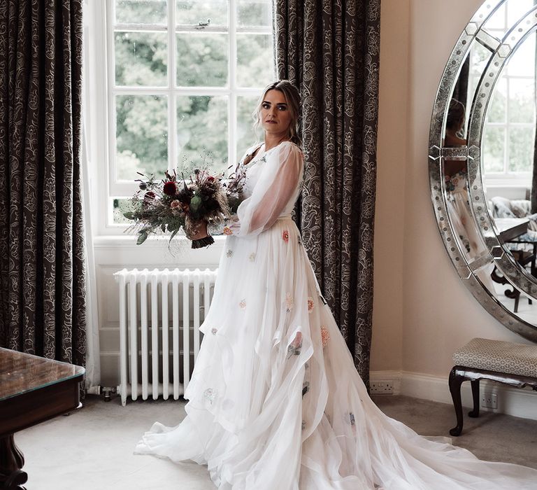 Bride in a Victoria Sanders embroidered wedding dress holding her dried and fresh flower bouquet by the window at Iscoyd Park 