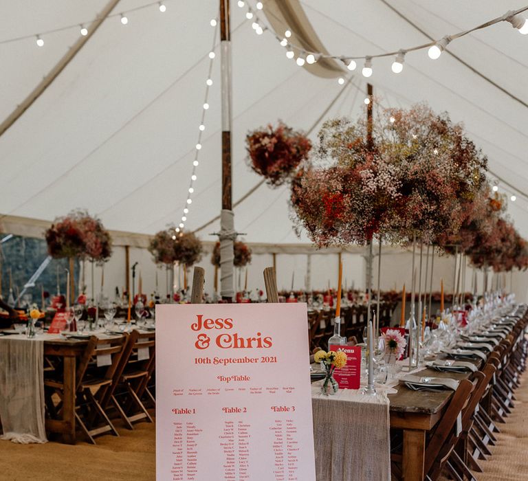 Marquee wedding reception with pink gypsophila flower clouds, festoon lights and a contemporary pink seating chart 