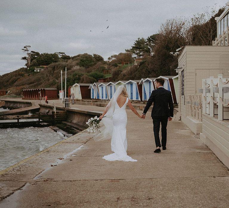 Bride and groom walk hand and hand along the seafront