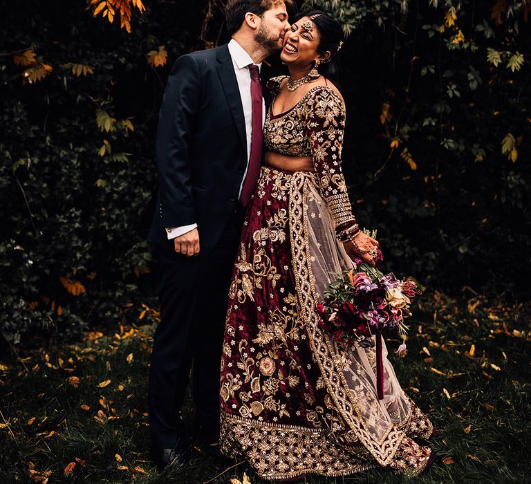 Grooms matches bride in his burgundy tie and dark suit as Bride wears Gold & Burgundy Indian saree wedding dress 