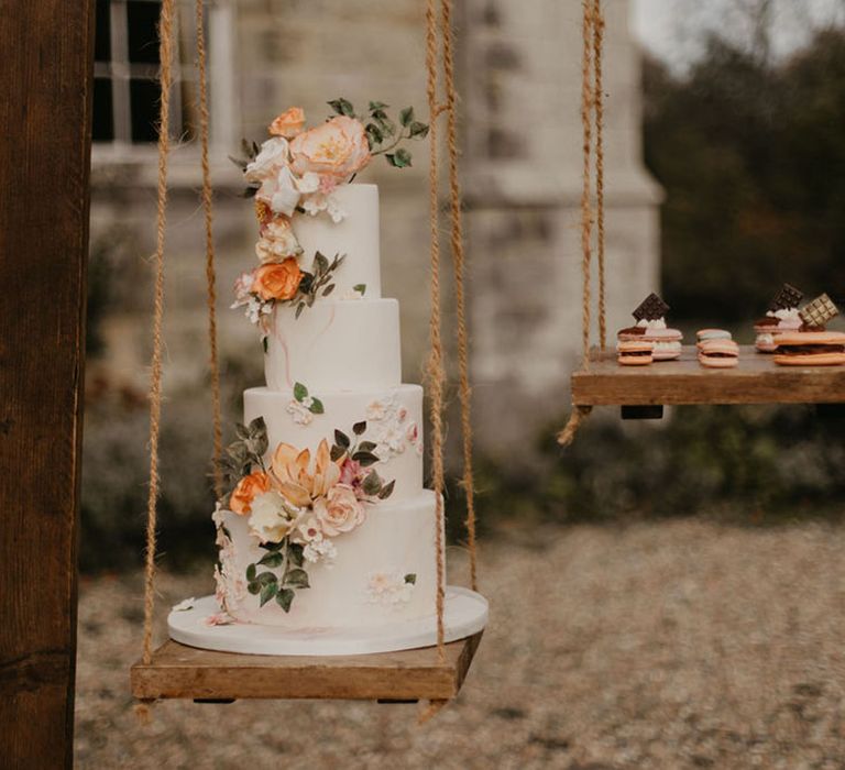 Four tier iced wedding cake with floral design on a swing wooden frame cake stand 