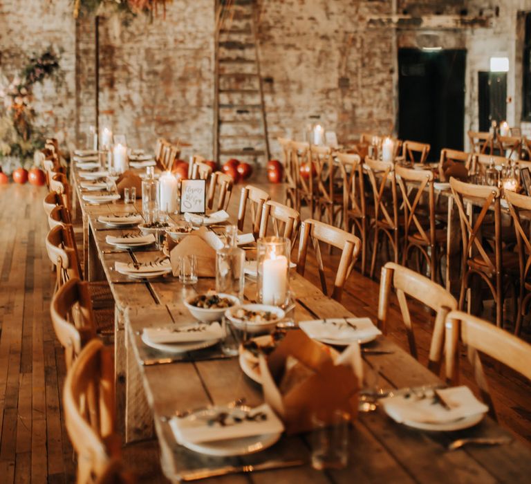 Long wooden tables and chairs in industrial style wedding reception room with exposed brick, bulb string lights and flower cloud for city centre wedding