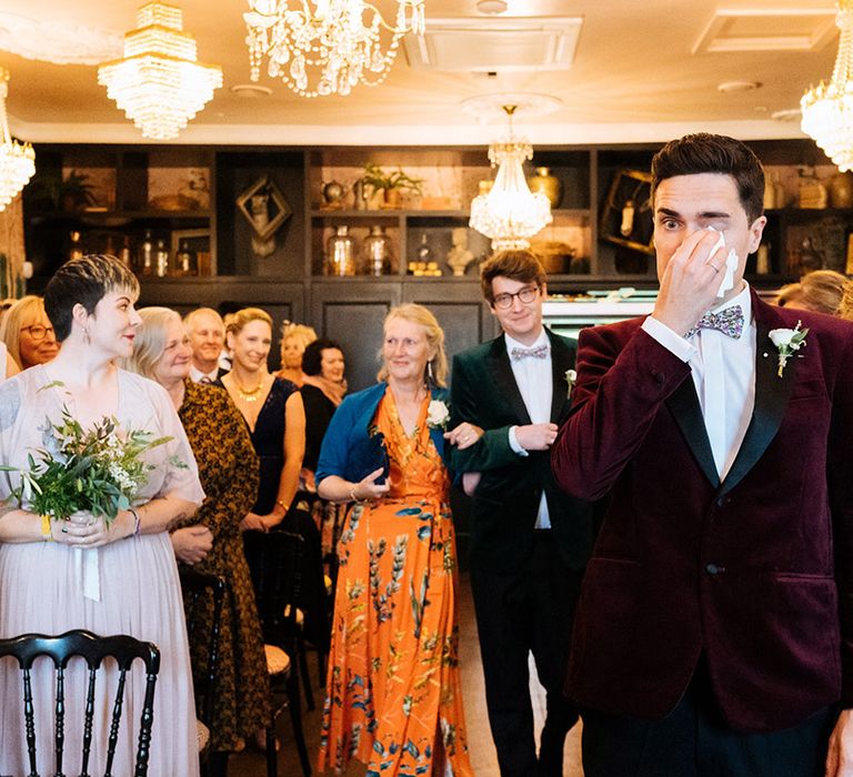 Groom wipes his eyes with tissue as the other groom is walked up the aisle by his mother