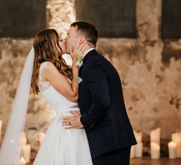 Groom in navy blue suit and bride in wedding skirt and top share a kiss