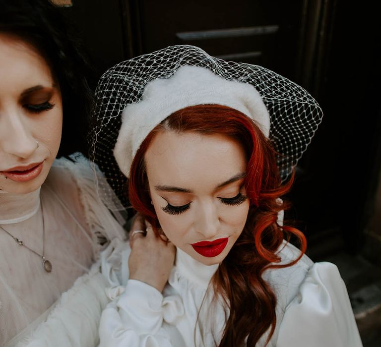 Bride in a high neck wedding dress with long sleeves wearing a berret with birdcage veil, red lipstick and false eyelashes 