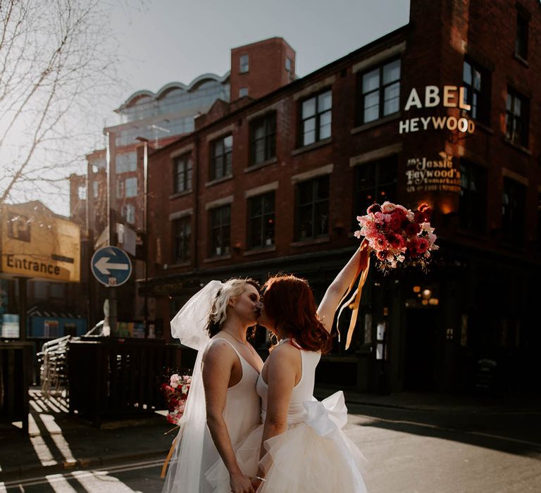 Manchester elopement with two brides kissing in a layered tulle skirt wedding dress and satin slip wedding dress with long bow veil 