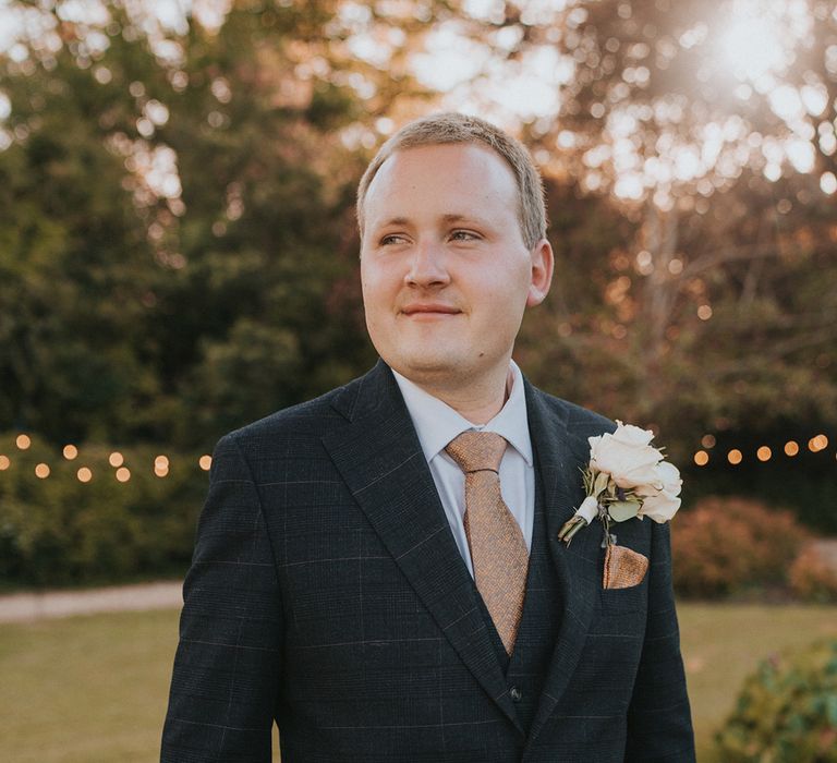 Groom in blue checkered suit with snake pattern tie and handkerchief with white rose and gypsophila boutonnière